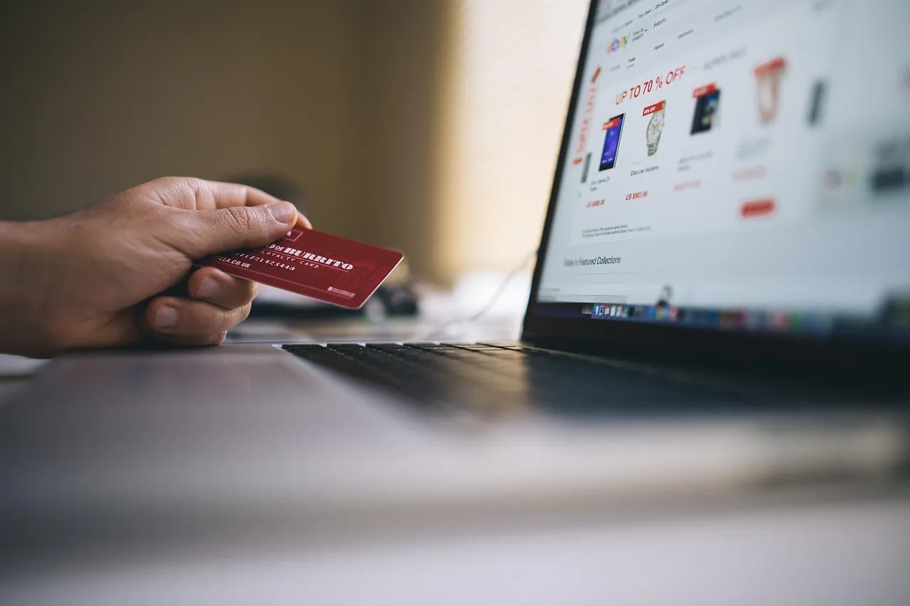 A person holds a red credit card while browsing an online store on a laptop.